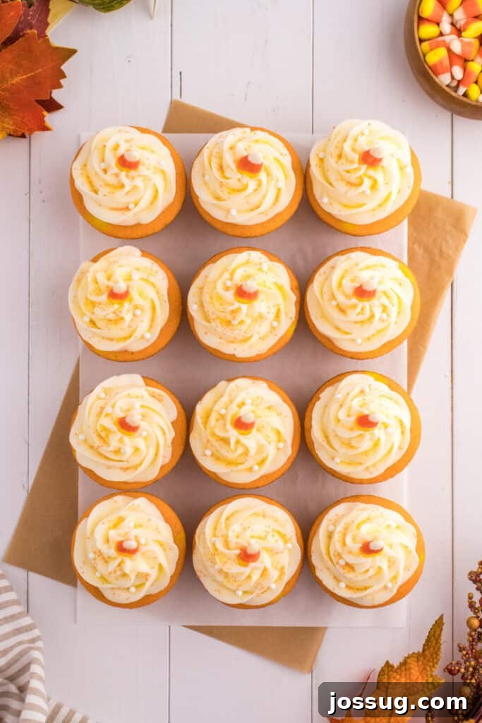 Overhead view of frosted Candy Corn Cupcakes arranged neatly on parchment with fall leaves and candy corn accents.