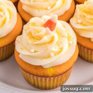 Square close-up of Candy Corn Cupcake topped with swirled white frosting, candy corn, and sugar pearls on a white plate.