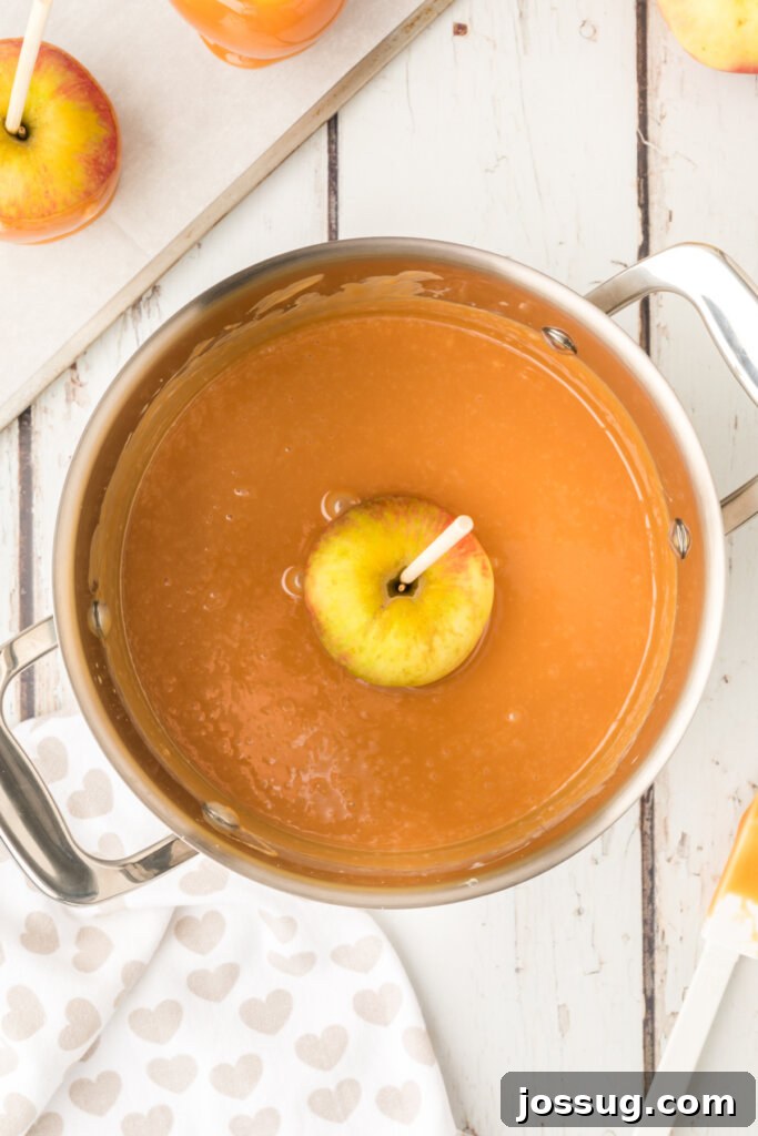 A crisp green apple being carefully dipped and coated in warm, glistening caramel sauce.