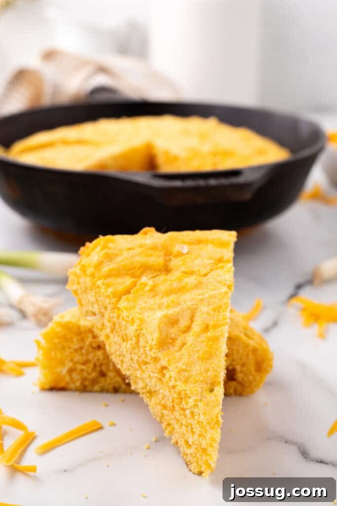 Savory Cheddar Onion Cornbread 2 Triangular slices of golden Cheddar Onion Cornbread stacked on a marble surface with the cast-iron skillet visible in the background.