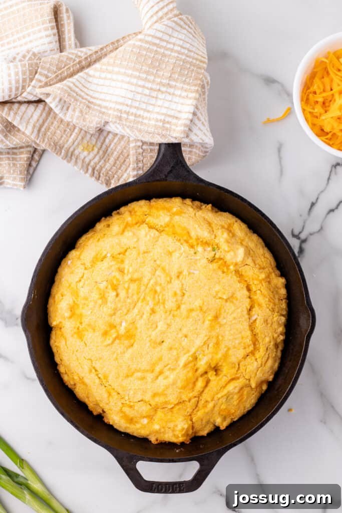 Savory Cheddar Onion Cornbread 11 Freshly baked Cheddar Onion Cornbread in a cast iron skillet with a golden top, cooling on a marble counter.