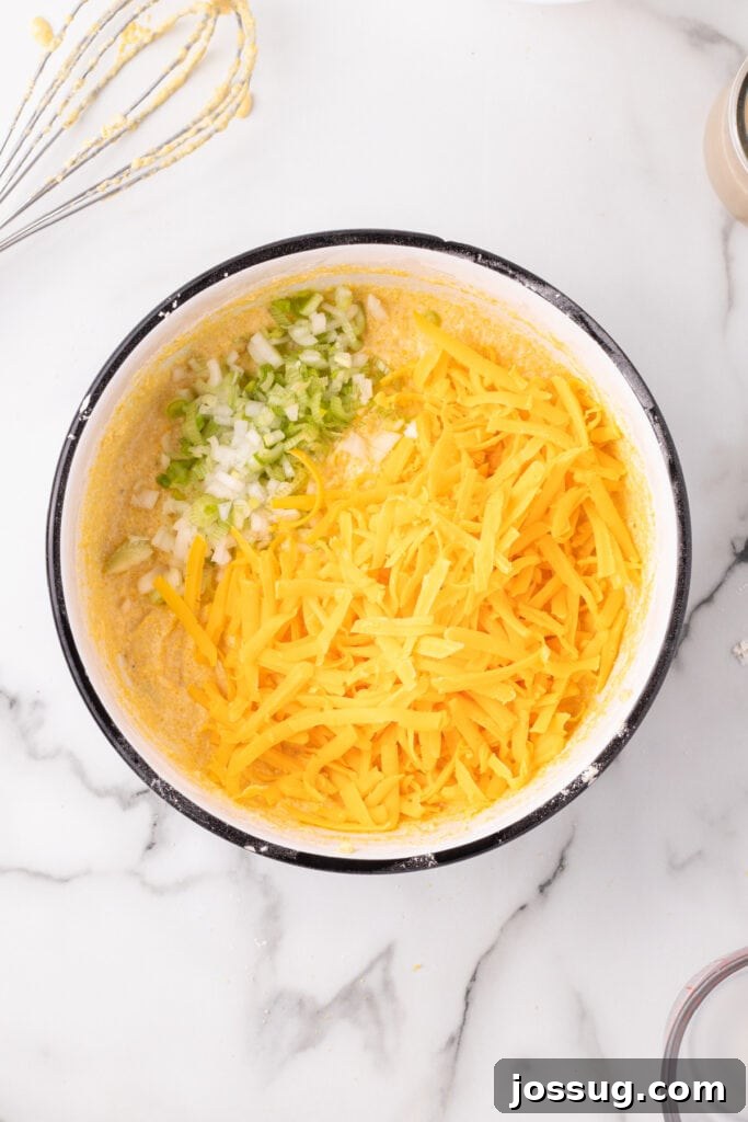 Savory Cheddar Onion Cornbread 7 Shredded Cheddar cheese and chopped green onions added to the cornbread batter in a mixing bowl.