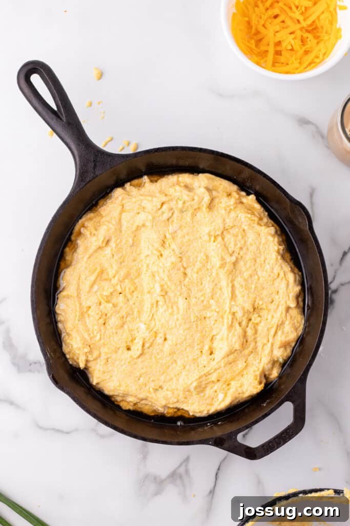 Savory Cheddar Onion Cornbread 10 Unbaked Cheddar Onion Cornbread batter spread evenly in a hot cast iron skillet, ready for baking.