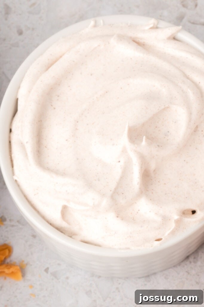 Close-up of fluffy spiced whipped cream with specks of cinnamon in a white ramekin.