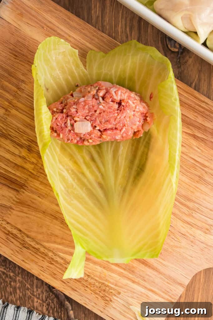 Spoonful of raw meat and rice filling placed in the center of a softened cabbage leaf on a wooden cutting board.
