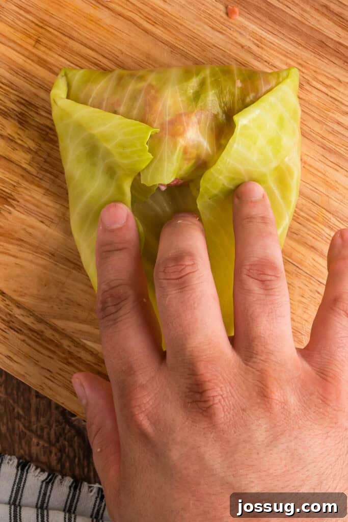 Hands folding sides of the cabbage leaf inward to secure the filling while rolling.