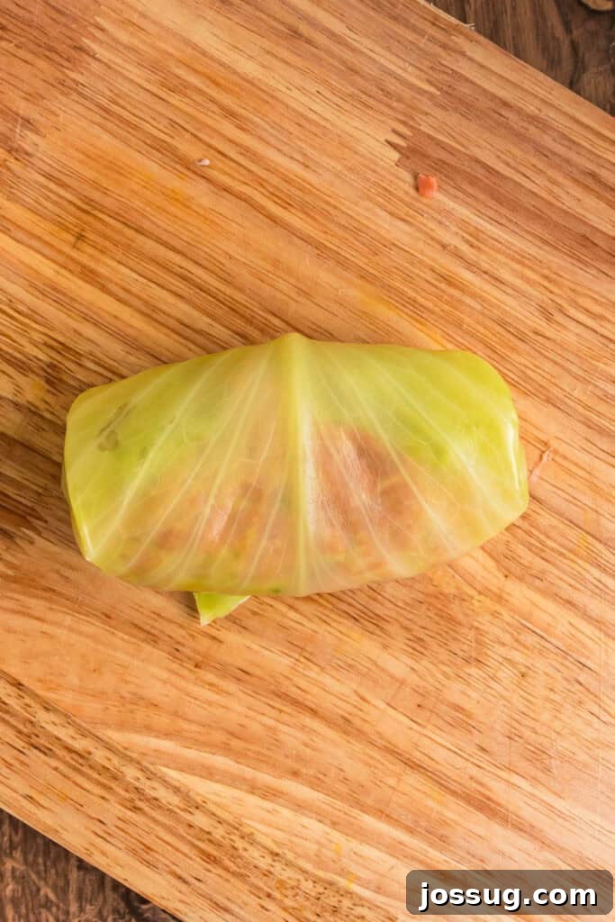 Fully rolled cabbage roll sealed and ready for baking, sitting on a wooden cutting board.