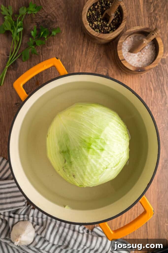 Whole green cabbage boiling in a large yellow-handled pot on a wooden surface with salt and pepper bowls nearby.