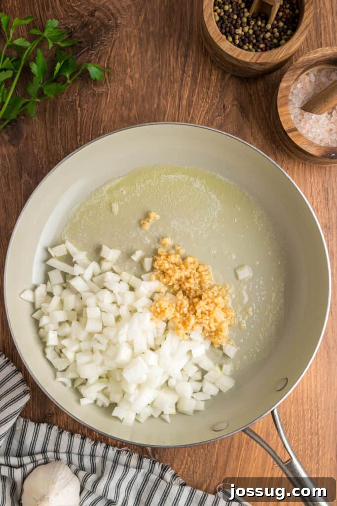 Skillet with melted butter, diced onions, and minced garlic beginning to sauté on a wooden surface.