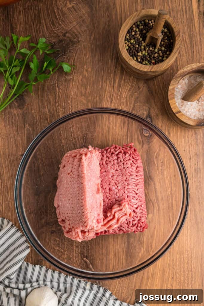 Glass mixing bowl with raw ground beef and ground pork placed side by side before mixing.