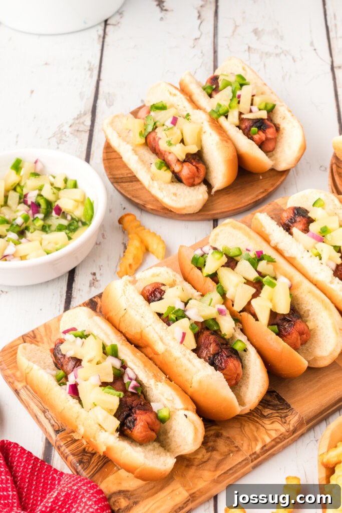 Four hawaiian hot dogs on a wooden board with a side of salsa