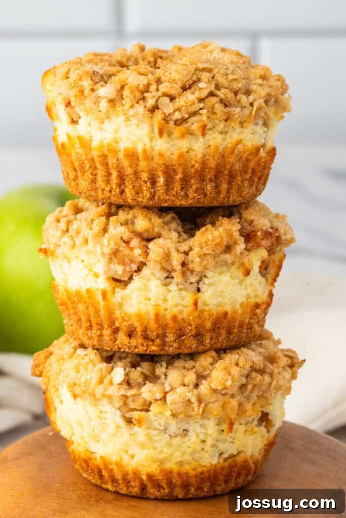 Spiced Apple Crumble Cheesecake Delights 2 A stack of three Mini Apple Crumble Cheesecakes showcasing their creamy cheesecake center, spiced apple layer, and golden oat crumble topping. The vibrant green of an apple is visible in the background.