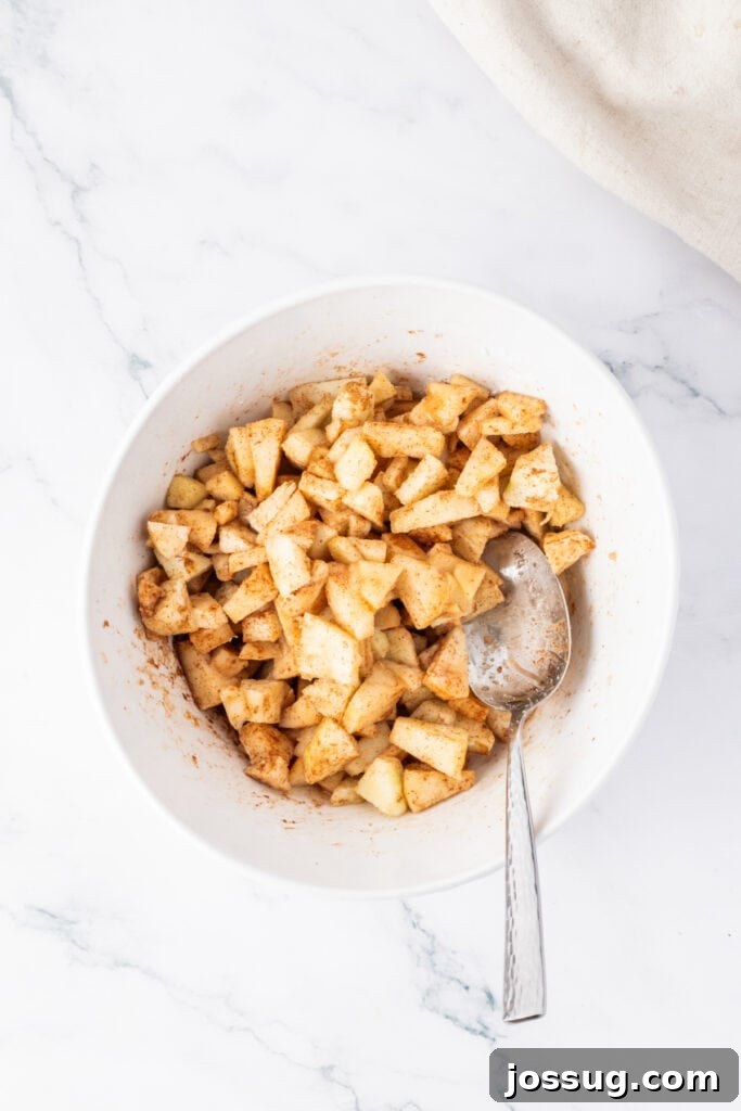 Spiced Apple Crumble Cheesecake Delights 12 A medium bowl containing finely diced apples mixed with granulated sugar, ground cinnamon, and vanilla extract, creating the aromatic and spiced apple layer.