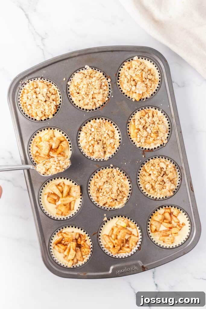 Spiced Apple Crumble Cheesecake Delights 15 A muffin pan with mini apple cheesecakes, each generously topped with the coarse oat crumble mixture before being placed into the oven for baking, ready to achieve a golden-brown crust.