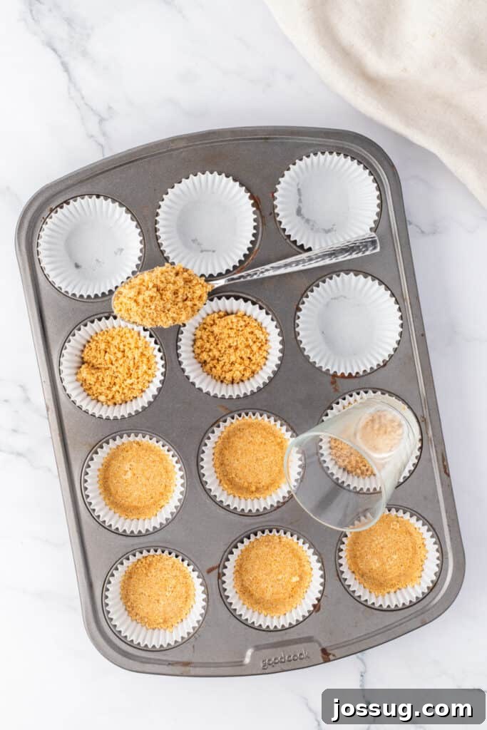 Spiced Apple Crumble Cheesecake Delights 7 A muffin pan neatly lined with cupcake wrappers, each filled with a portion of the graham cracker crust mixture being pressed firmly down with the flat bottom of a small glass, creating a compact base.