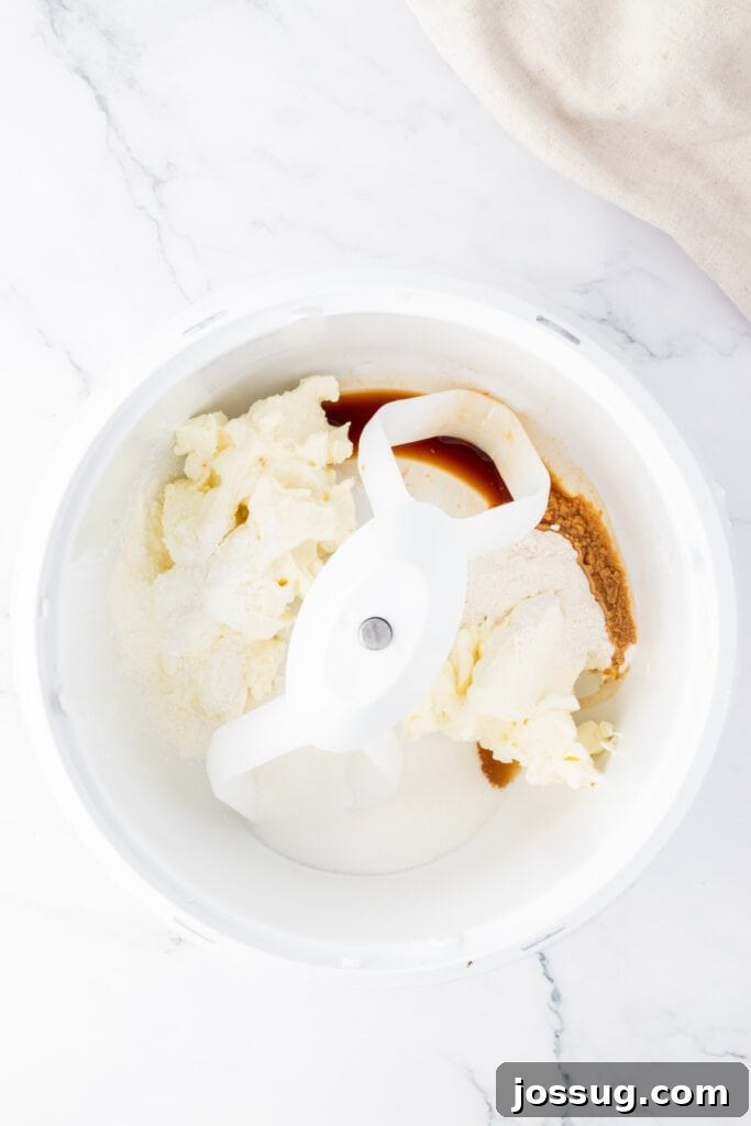 Spiced Apple Crumble Cheesecake Delights 8 A stand mixer bowl filled with softened cream cheese, granulated sugar, a tablespoon of all-purpose flour, and vanilla extract, prepared for blending into the smooth and creamy cheesecake filling.