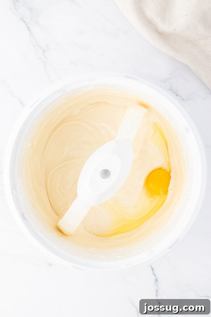 Spiced Apple Crumble Cheesecake Delights 9 Smooth and creamy cheesecake batter in a large mixing bowl, with one whole egg being carefully added for the final stage of mixing the filling.