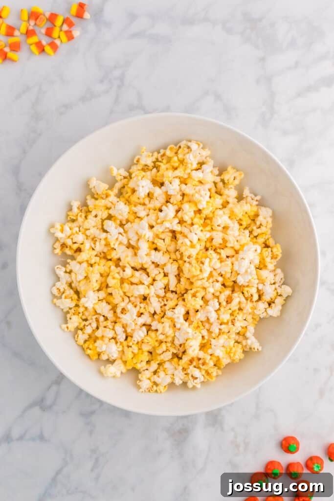 Monster Munch Popcorn 4 Large white bowl filled with freshly popped popcorn on a marble countertop with candy corn and pumpkins scattered around.