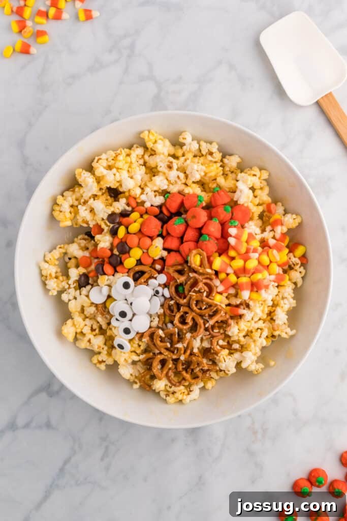 Monster Munch Popcorn 7 Popcorn in a mixing bowl topped with pretzels, candy corn, candy pumpkins, Reeseās pieces, and candy eyeballs before stirring.