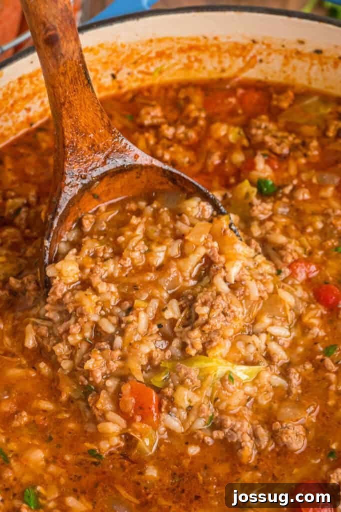 A wooden ladle lifting a hearty scoop of Cabbage Roll Soup, showcasing tender rice, savory beef, diced tomatoes, and soft cabbage in the rich broth.