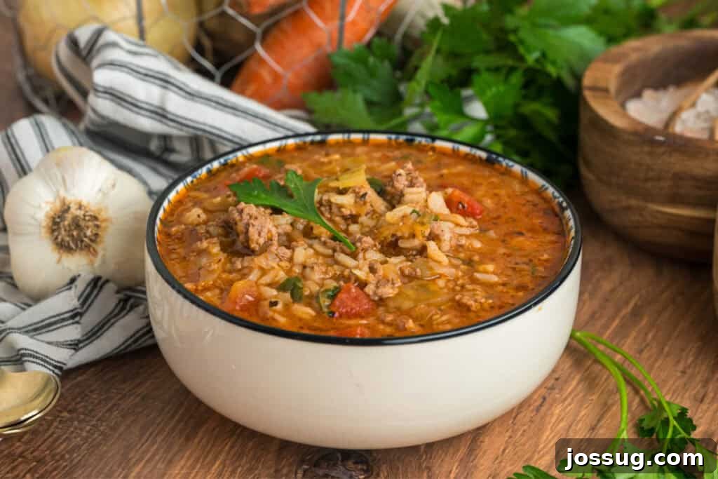 Side view of a steaming bowl of cabbage roll soup beautifully garnished with fresh parsley, with rustic kitchen props like garlic and herbs subtly blurred in the background.