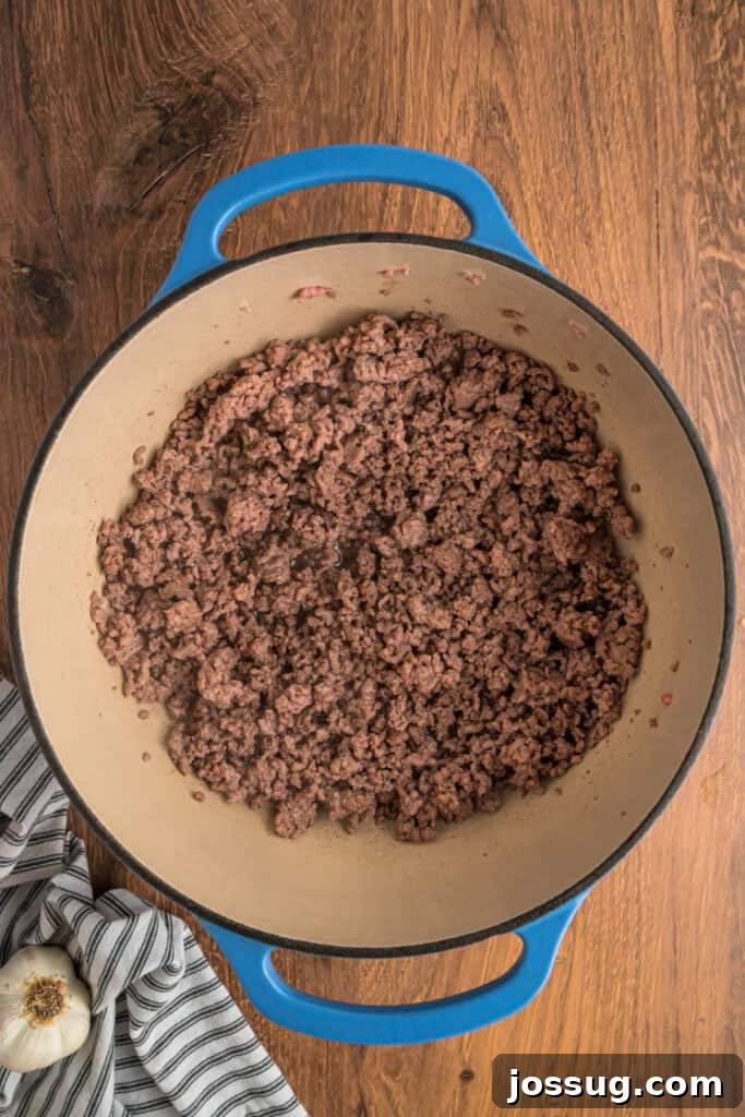 Cooked and crumbled ground beef and pork in a blue dutch oven after browning thoroughly.