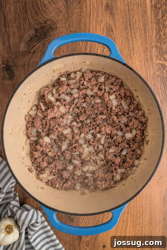 Cooked ground meat mixture with softened onions and garlic, creating an aromatic base in a blue dutch oven.