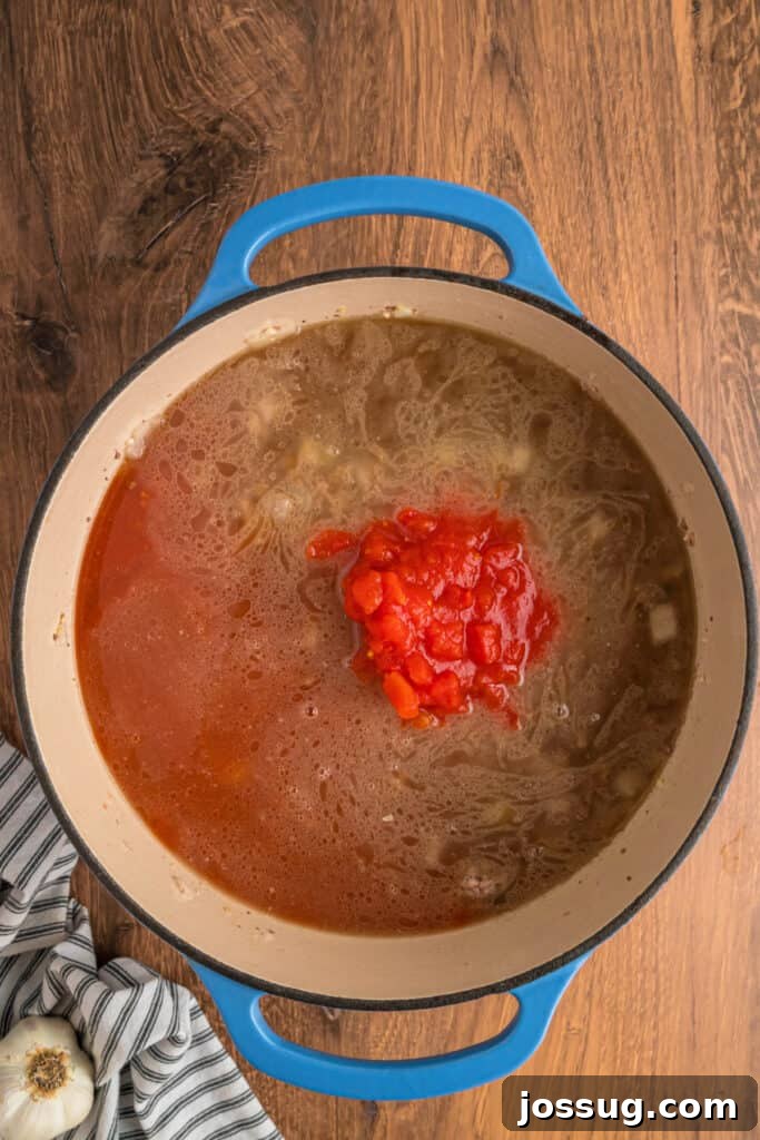 Beef broth, V8 vegetable juice, and canned diced tomatoes poured into the meat mixture, creating a rich liquid base in the pot.