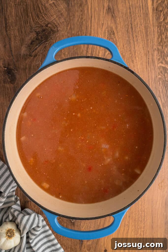 The tomato broth mixture simmering gently in a blue dutch oven, infusing the meat and aromatics with flavor.