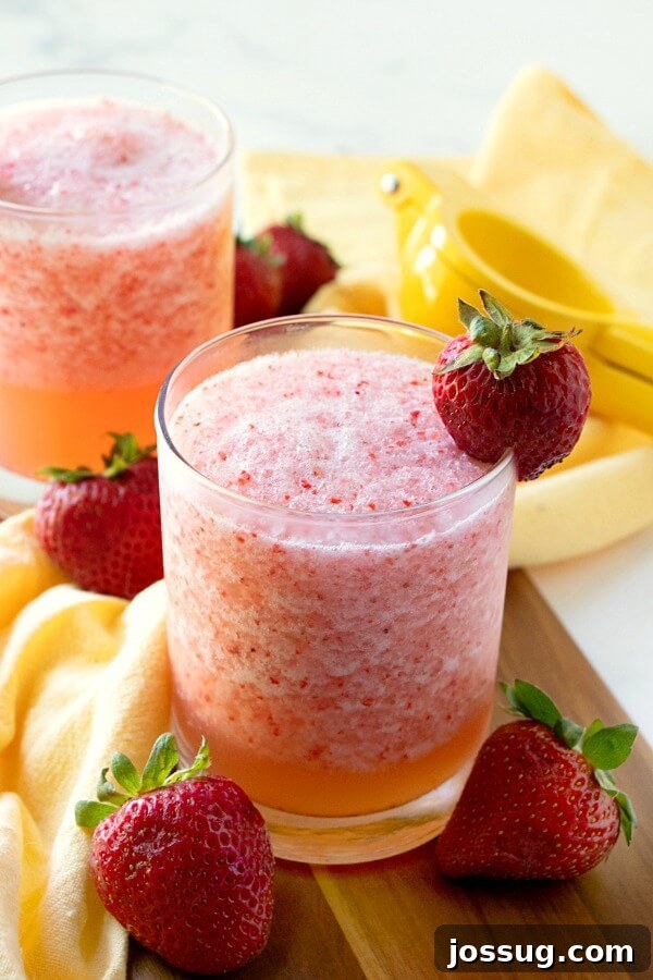 Zesty Berry Fruit Freeze 3 Two glasses filled with bright red Lemon Berry Fruit Slush, each garnished with a fresh strawberry, on a light background.
