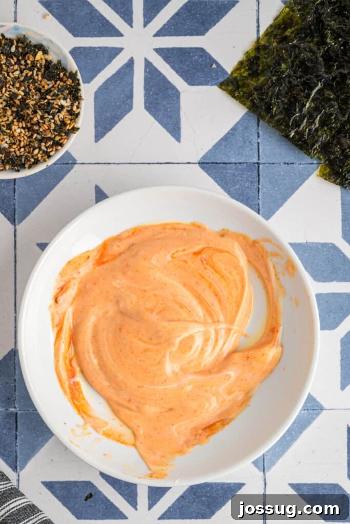 Homemade Sushi Bake Delight 11 Sriracha mayo mixture swirled together in a bowl, forming a creamy orange sauce for drizzling.