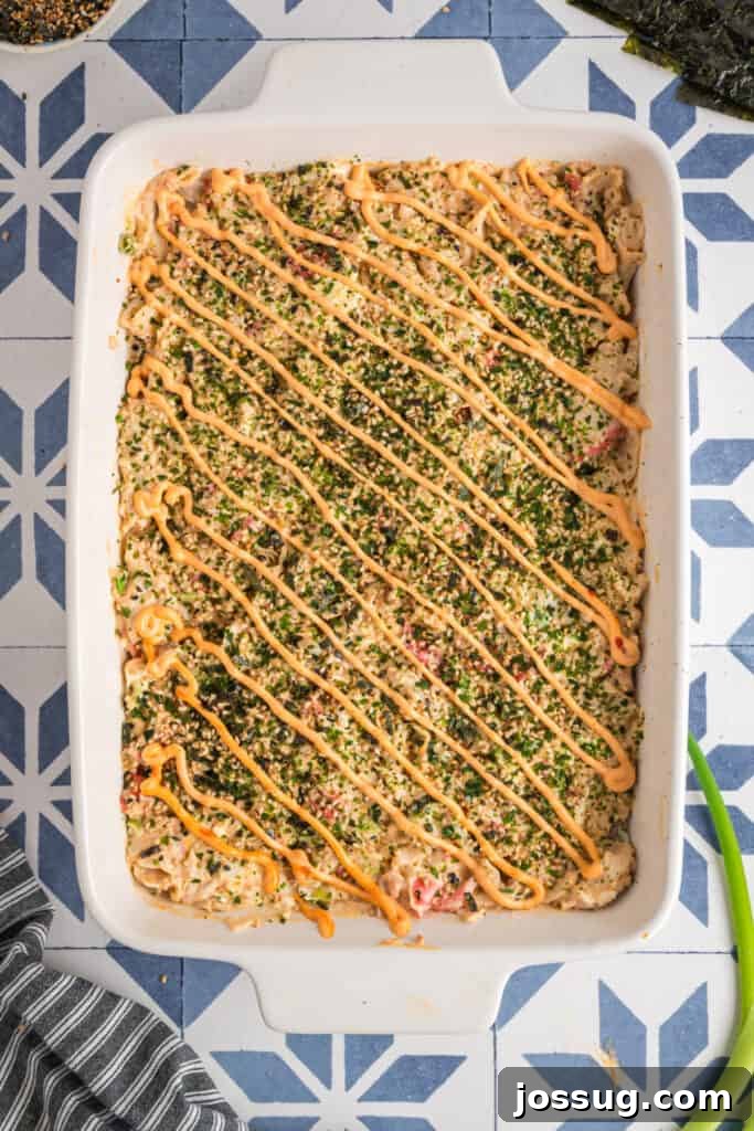 Homemade Sushi Bake Delight 12 Finished sushi bake in a white baking dish topped with furikake and drizzled with sriracha mayo in neat diagonal lines.