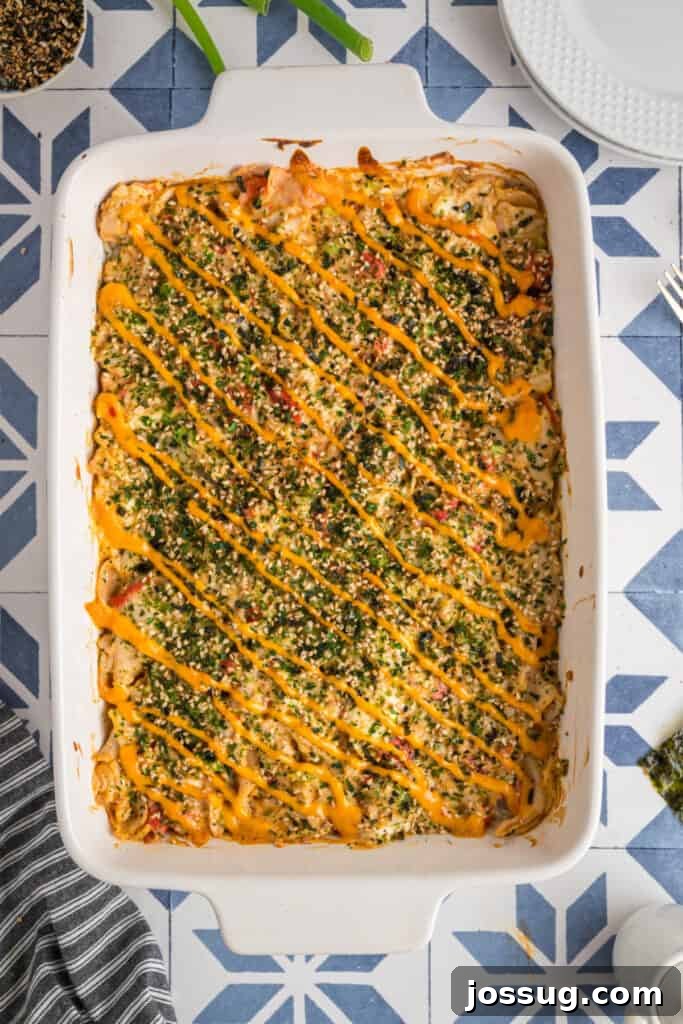 Homemade Sushi Bake Delight 13 Baked sushi casserole in a white dish topped with furikake and drizzled with sriracha mayo, ready to serve.