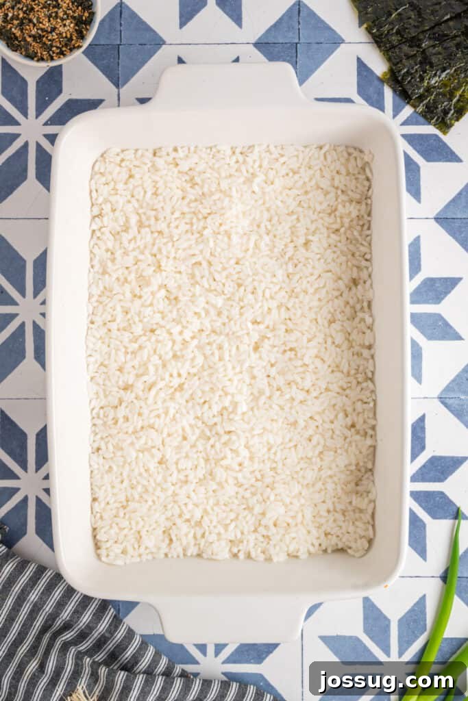 Homemade Sushi Bake Delight 6 Baking dish with a layer of cooked sushi rice spread evenly across the bottom, ready for topping.