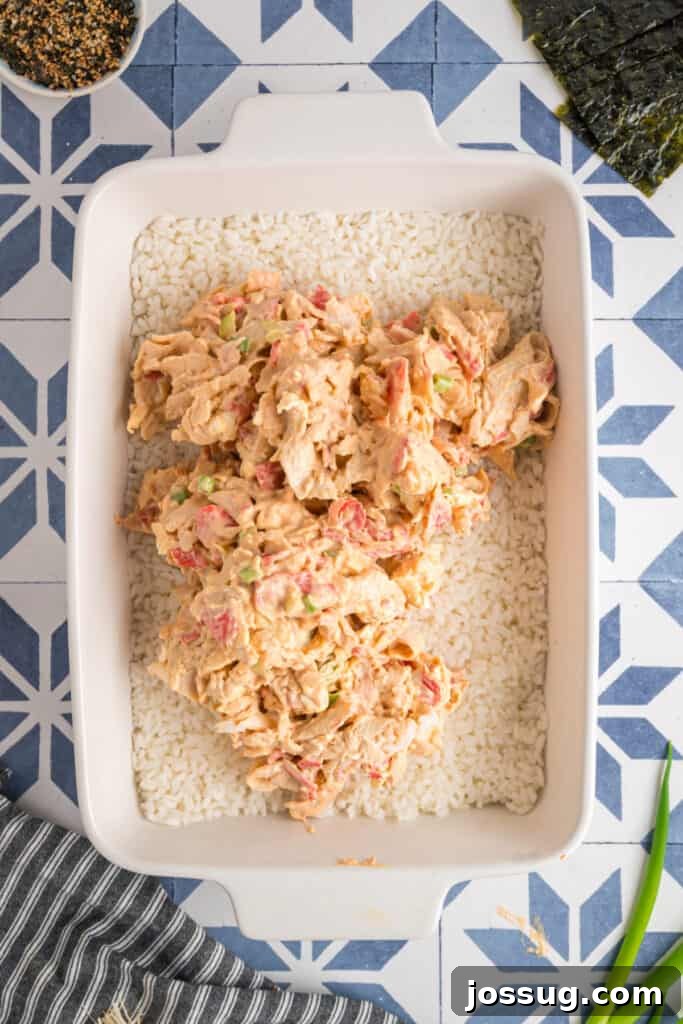 Homemade Sushi Bake Delight 7 Sushi bake being assembled with the creamy crab mixture spooned over the rice layer in a baking dish.