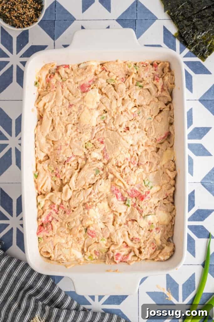Homemade Sushi Bake Delight 8 Sushi bake filling evenly spread over the rice in a casserole dish, showing creamy texture and bits of crab and green onion.