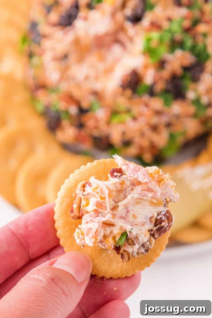 Hand holding a cracker topped with a bite of creamy Holiday Cheese Ball.