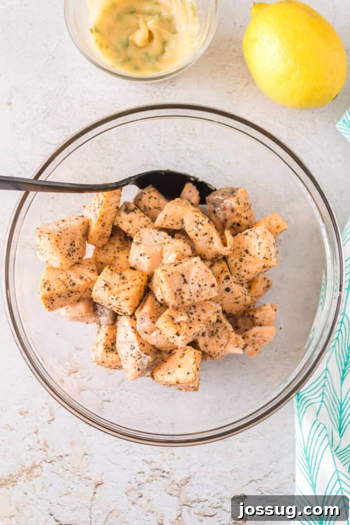 Bowl of freshly cooked salmon bites beside a lemon and bowl of garlic butter mixture.