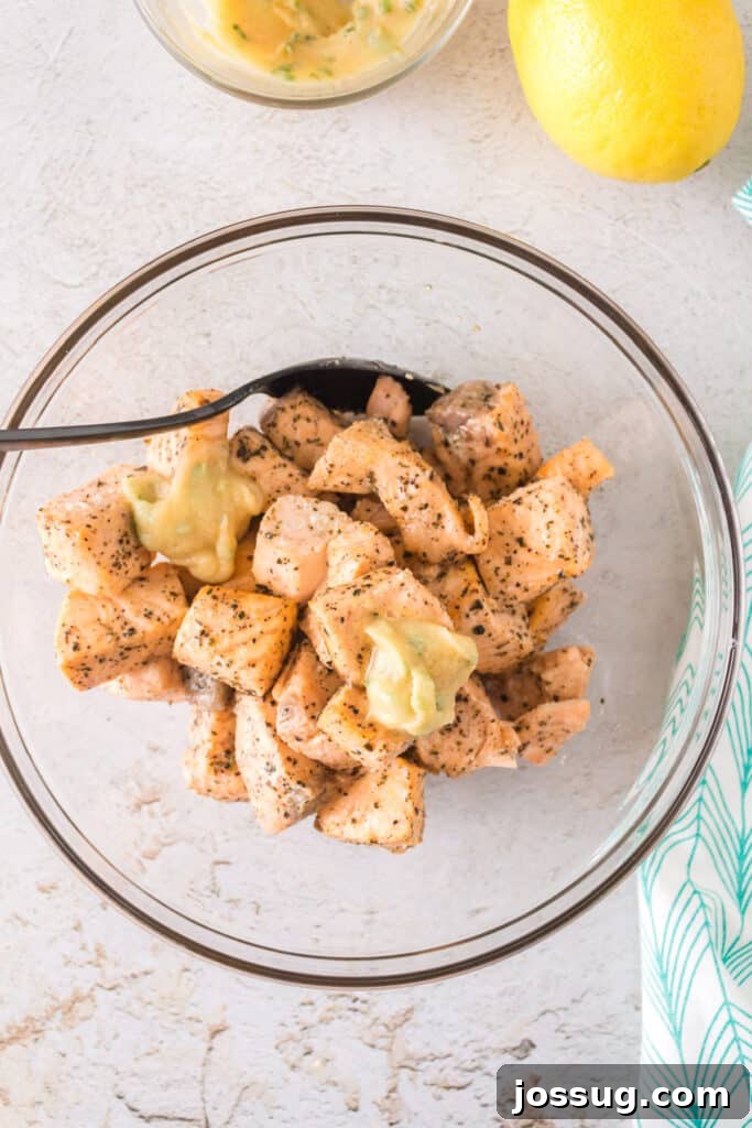 Salmon bites being drizzled with melted garlic butter in a clear mixing bowl.