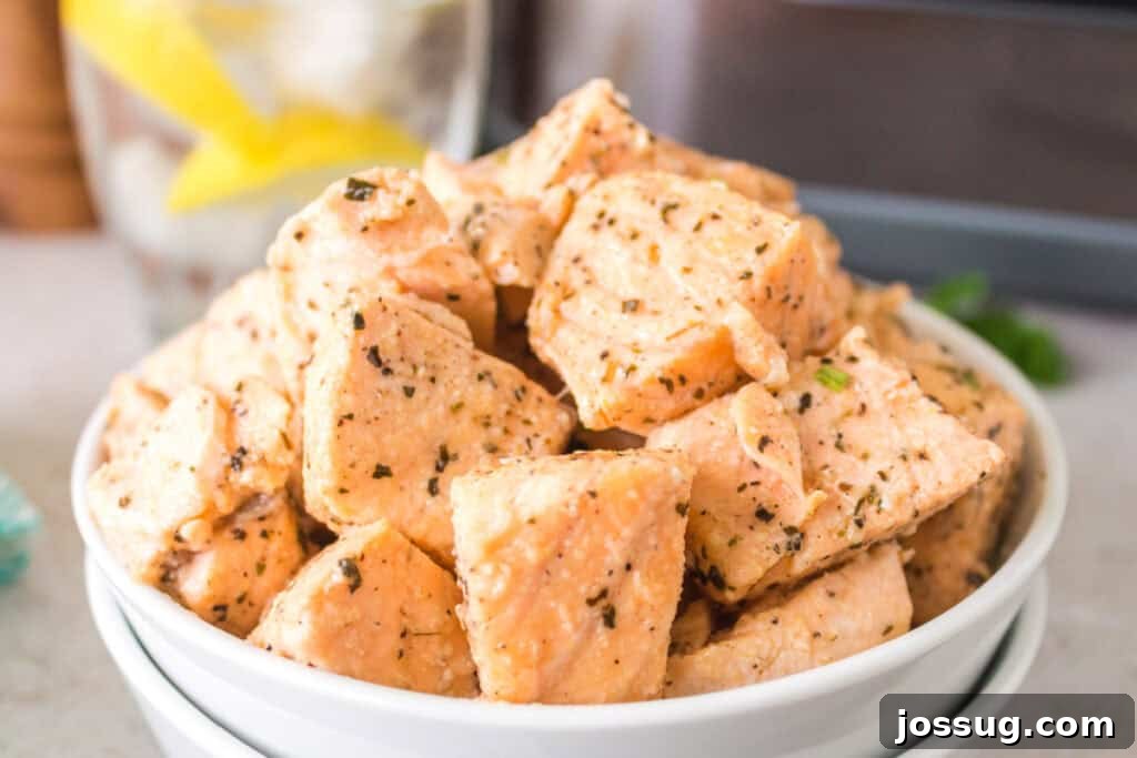 White bowl filled with seasoned, air-fried salmon bites on a countertop with an air fryer in the background.