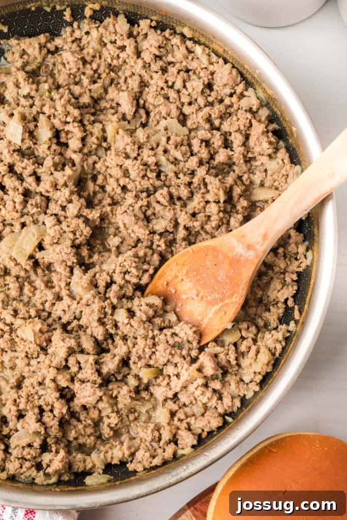 Maid-Rite loose meat sandwich filling cooking in a skillet with a wooden spoon.