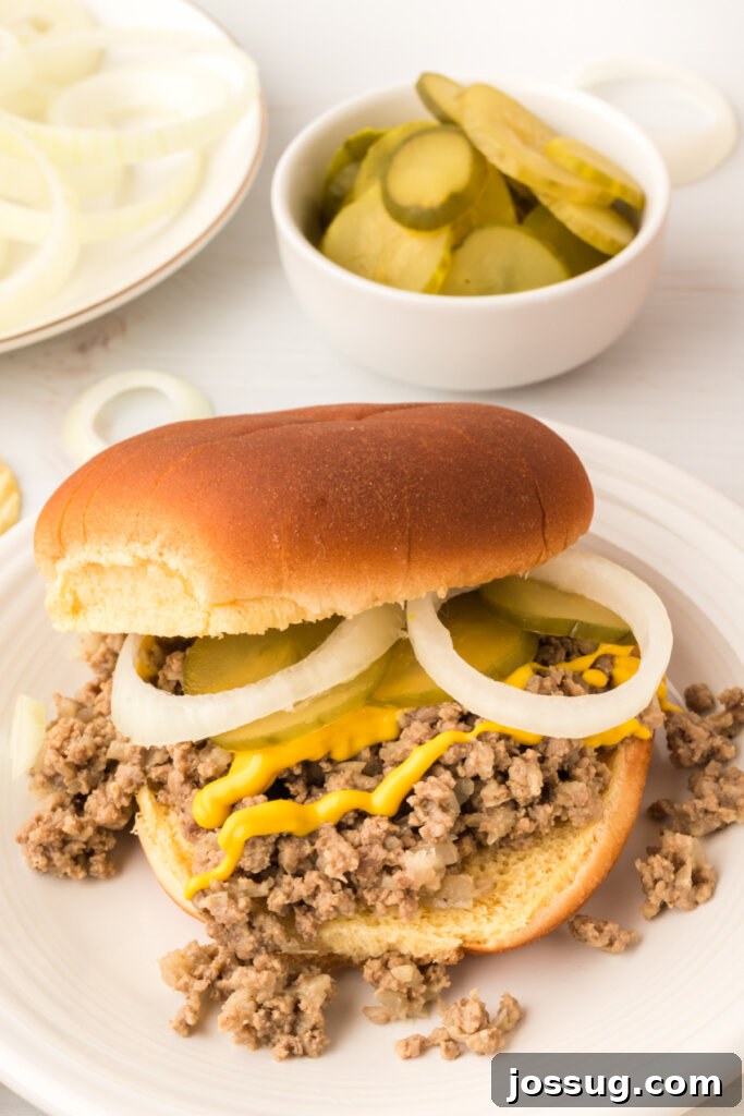 A Maid-Rite sandwich garnished with onions, pickles, and mustard on a plate.