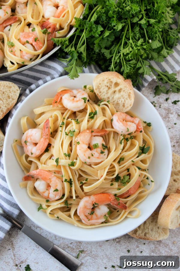 A close-up view looking down into a bowl of finished shrimp scampi with pasta, garnished with fresh parsley.