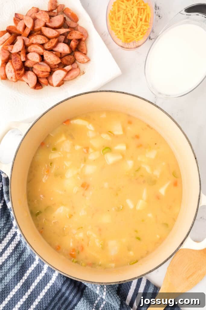 Soup simmering in a large pot with potatoes and vegetables, with browned sausage, shredded cheese, and milk set aside.