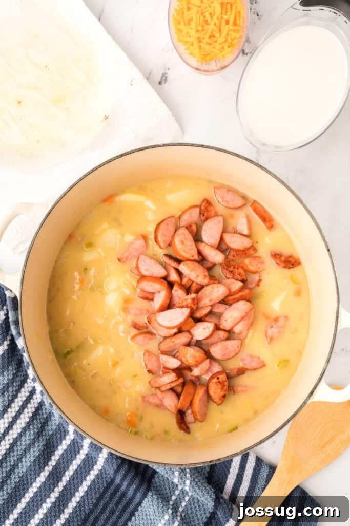 Cooked kielbasa sausage being added back into the pot of creamy potato soup.