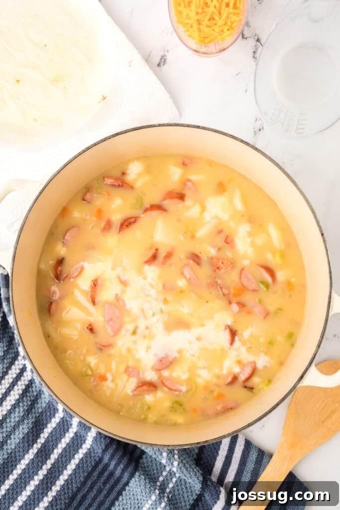 Milk poured into the pot of sausage and potato soup, creating a creamy base.
