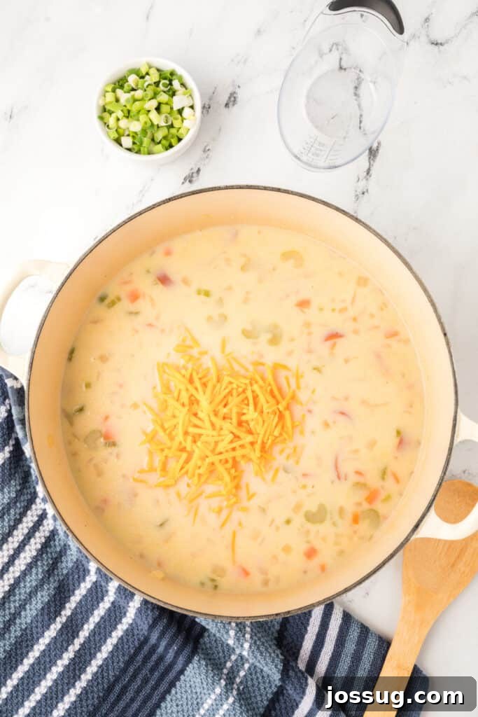 Shredded cheddar cheese sprinkled into the pot of creamy soup, ready to melt.