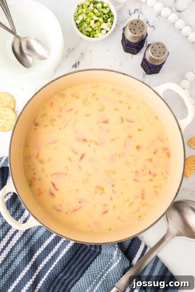 Finished pot of cheesy kielbasa potato soup with green onions and cheese nearby for garnish.