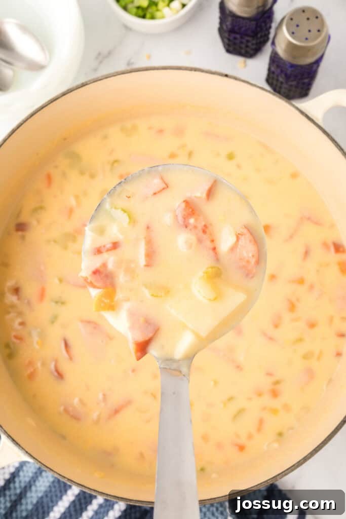 Ladle lifting a hearty serving of cheesy kielbasa potato soup filled with sausage, potatoes, and vegetables.