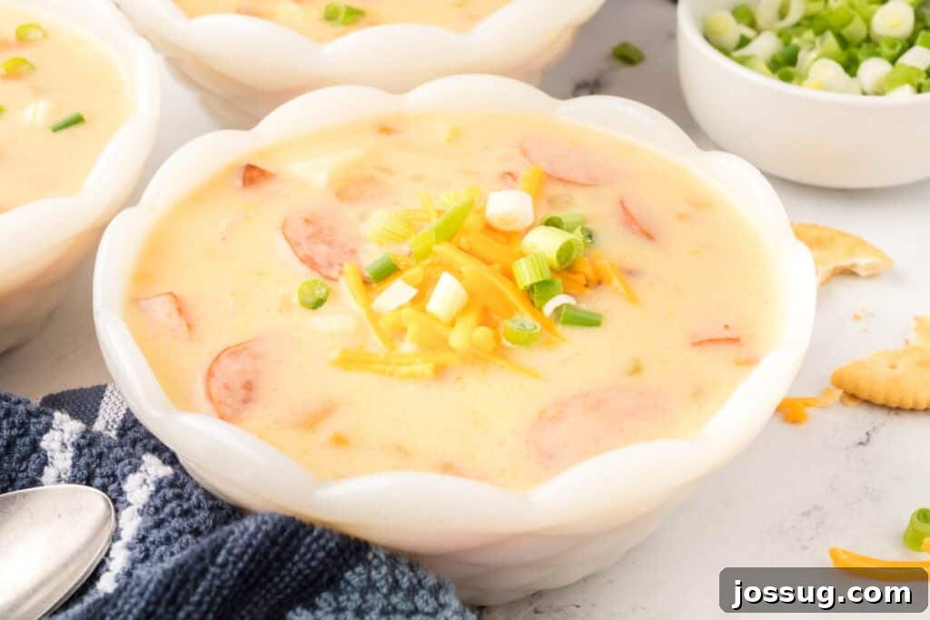 Close-up ladle full of cheesy kielbasa potato soup showing sausage slices, potatoes, and creamy broth.